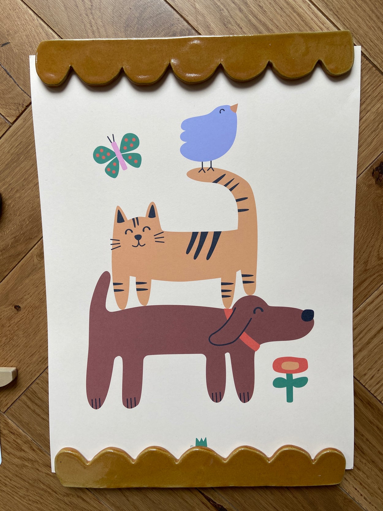 Porte affiche marron contenant une affiche reprensentant un chien portant un chat portant un oiseau