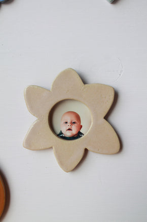 Cadre photo nacré en forme de fleur. 
En son centre se tient une photo d'une tête de bébé